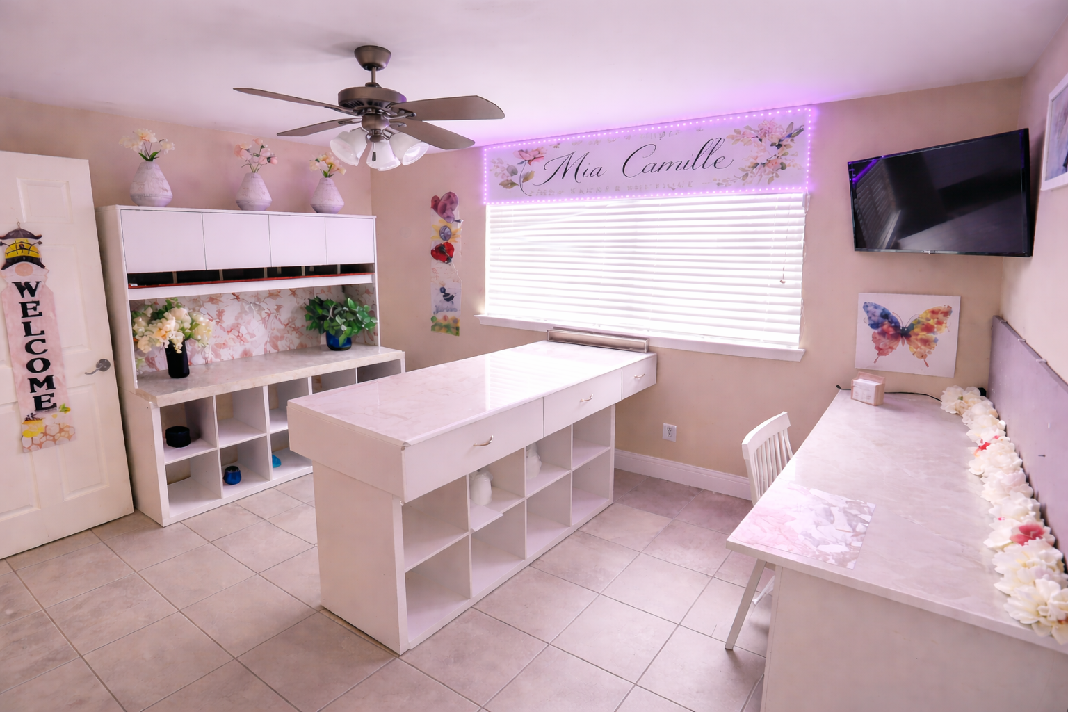 Inside the Mia Camille floral design studio — white work tables, cubby shelving, and the Mia Camille banner lit in pink